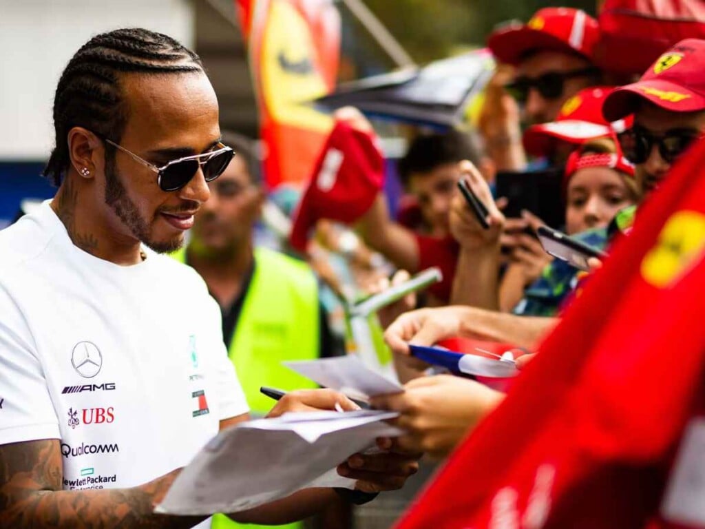 Lewis Hamilton signing autographs amidst a Ferrari flag